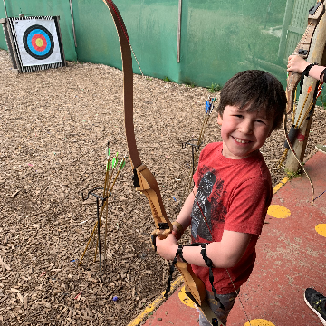 A boy holding a bow and arrow near an archery target