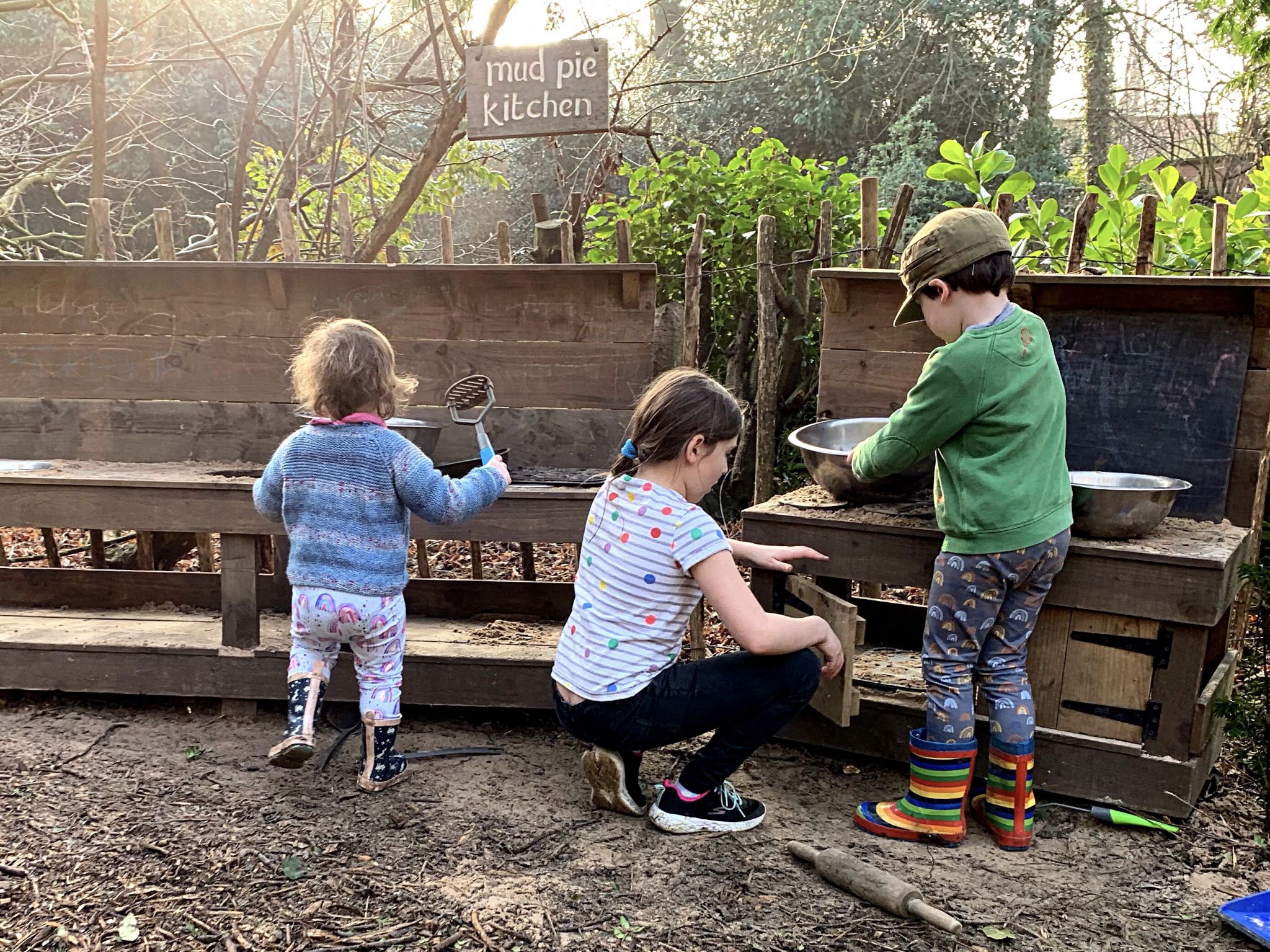 3 children playing in a mud kitchen
