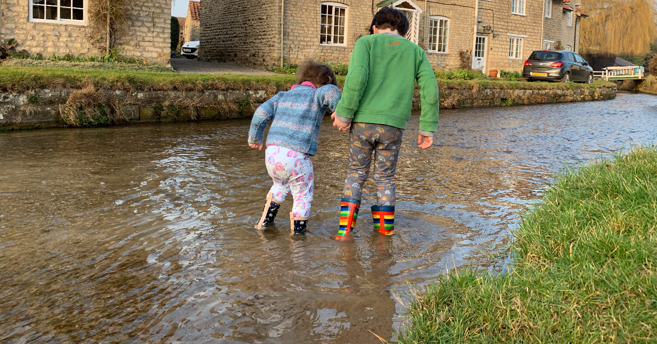 two young children splashing in wellies in the river