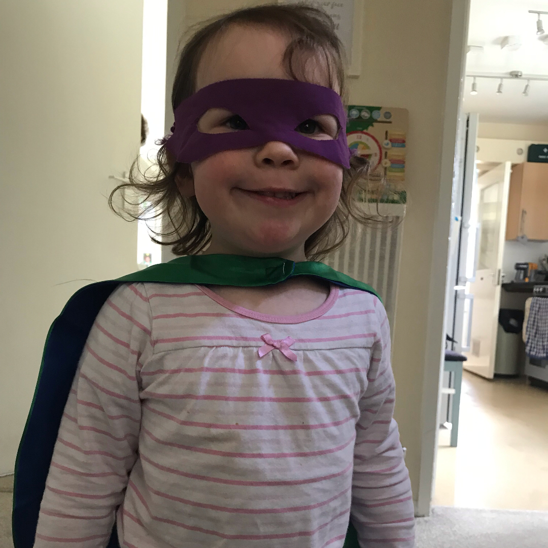 A girl dressed as a superhero with cape and mask