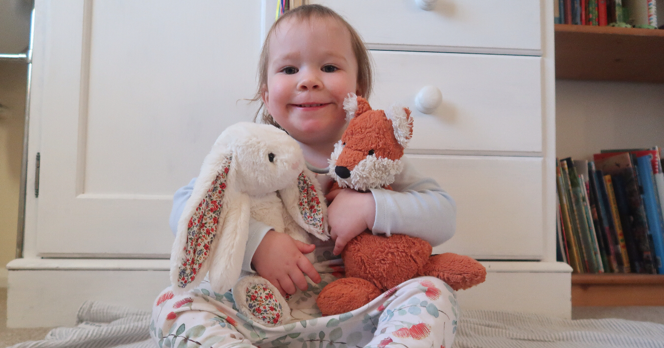 a toddler girl hugging a cuddly toy fox and bunny