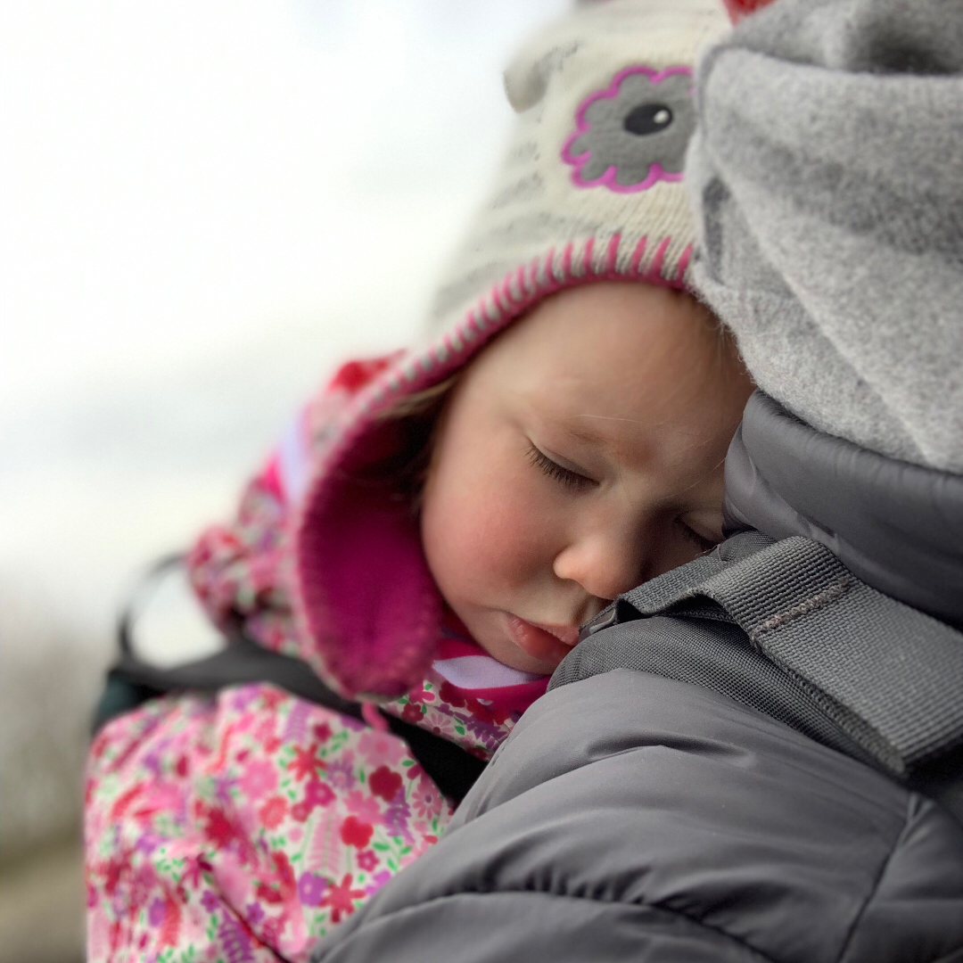 A toddler sleeping outside in a baby carrier