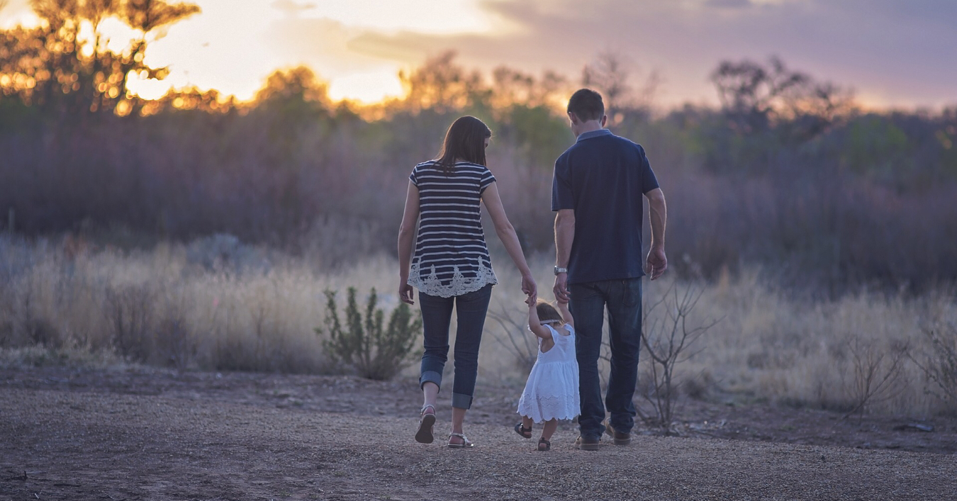 parents walking with a small child into the sunset 