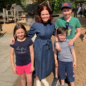 3 children standing smiling with Lindsey a Blue Peter Presenter