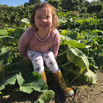 A child sat grinning in a veg patch