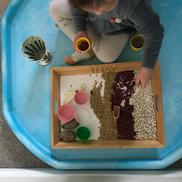a child sat in a tuff tray scooping beans for a Christmas toddler activity