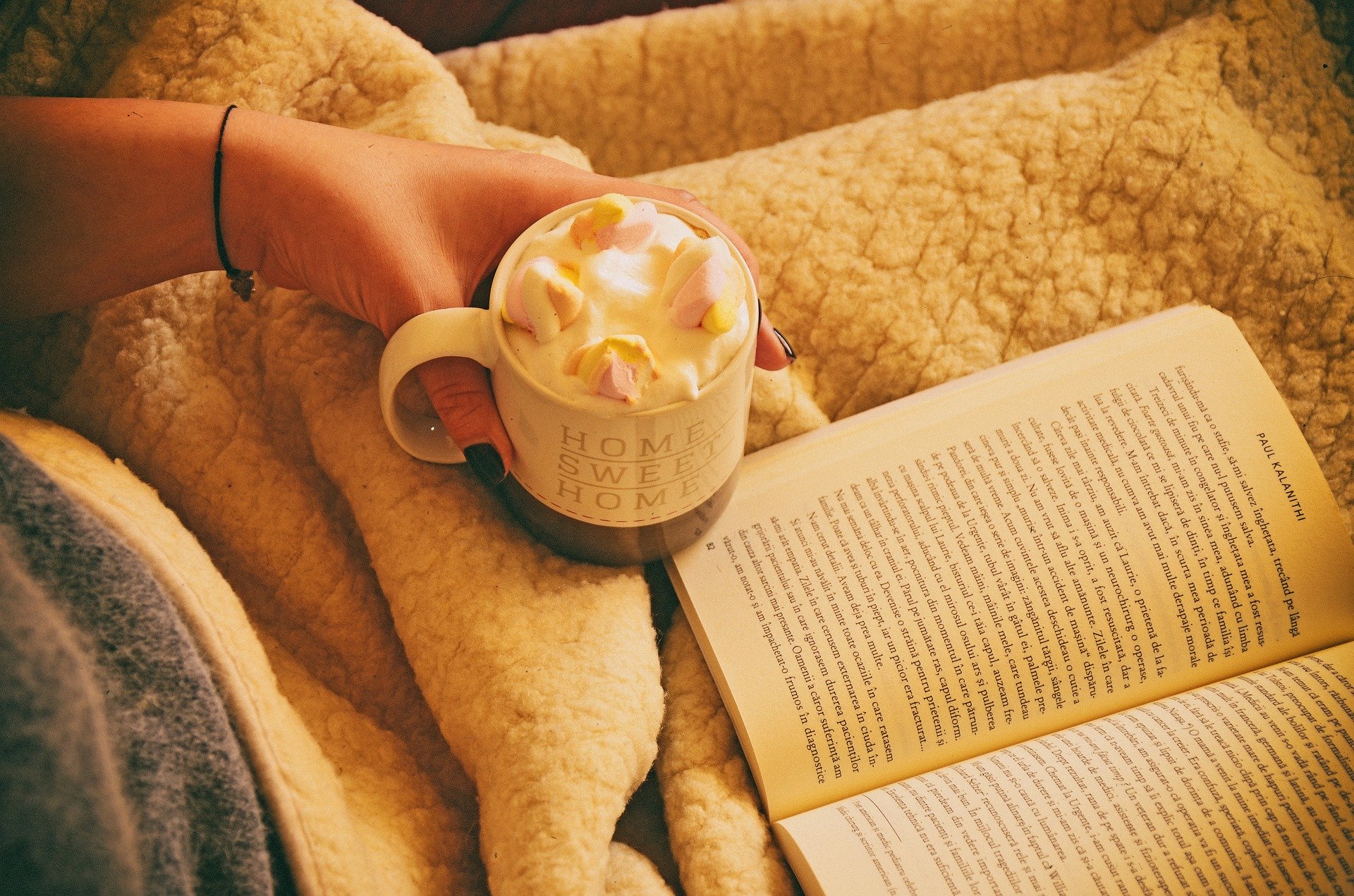 a lady sat under a blanket with a hot chocolate and a book