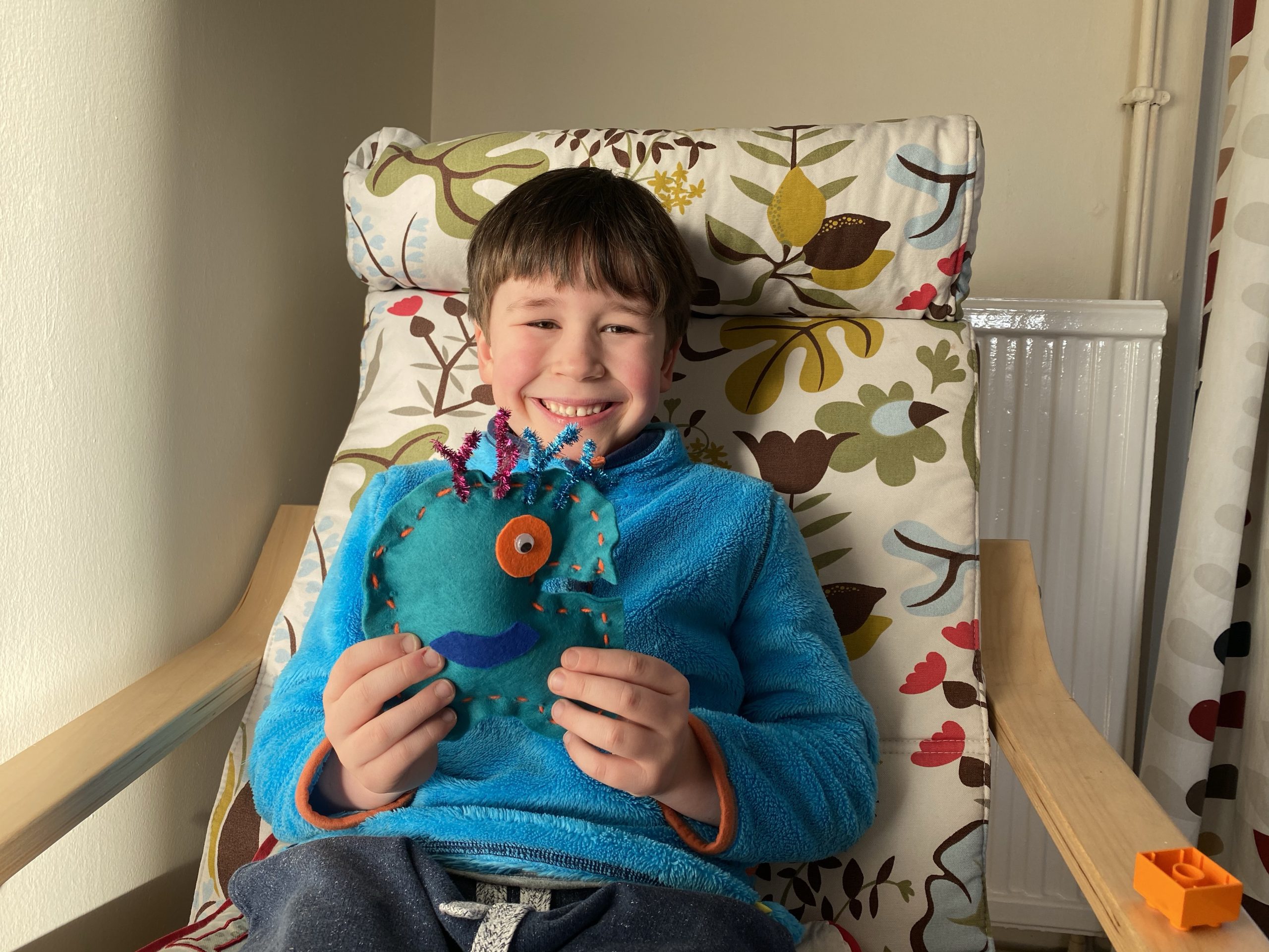 A boy holding up a sew your own alien whilst smiling 