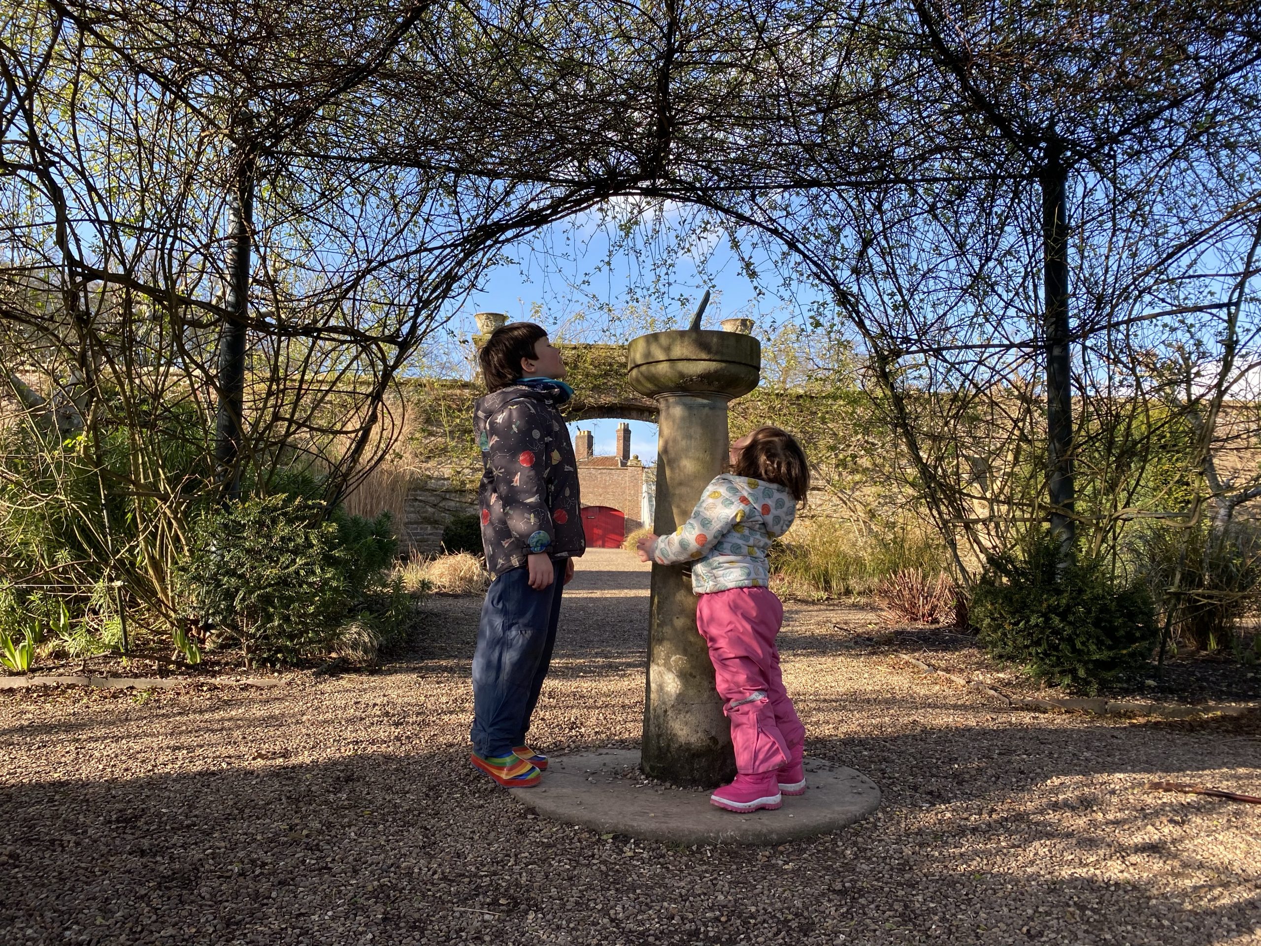 Two small children playing by a sun dial in a garden