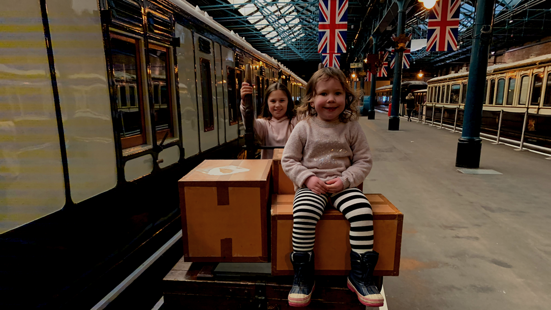 2 children on a luggage cart by a train