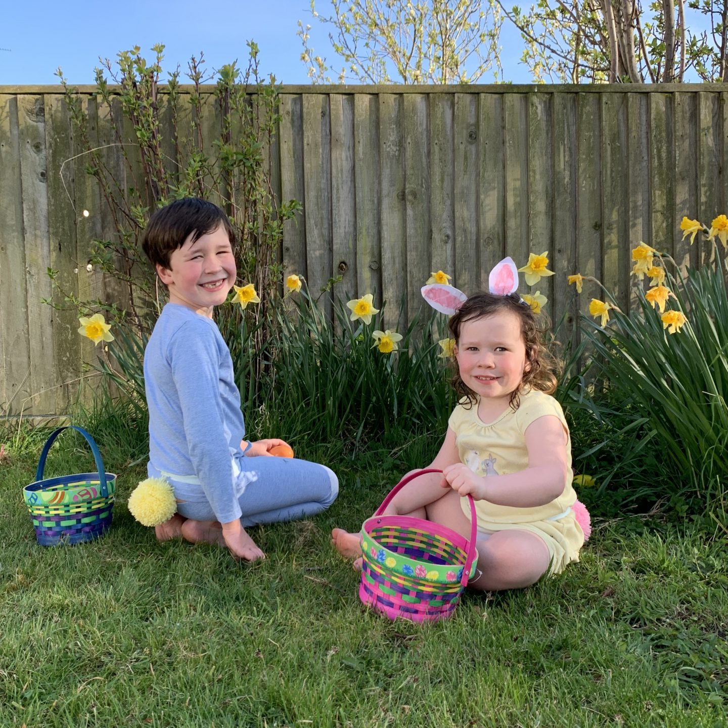 Two children collecting eggs with bunny tails and baskets