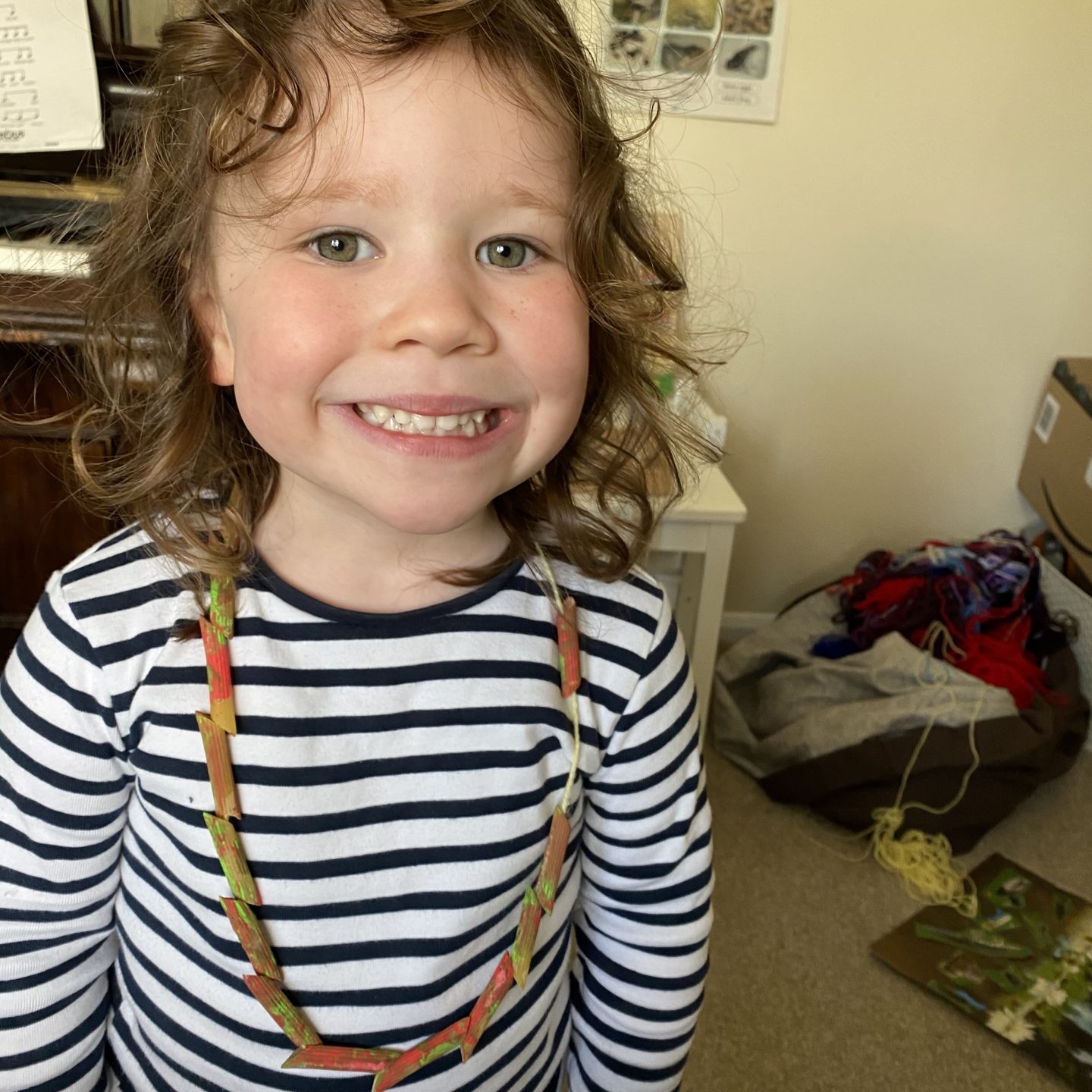 A girl showing off her homeschool creations of a pasta necklace