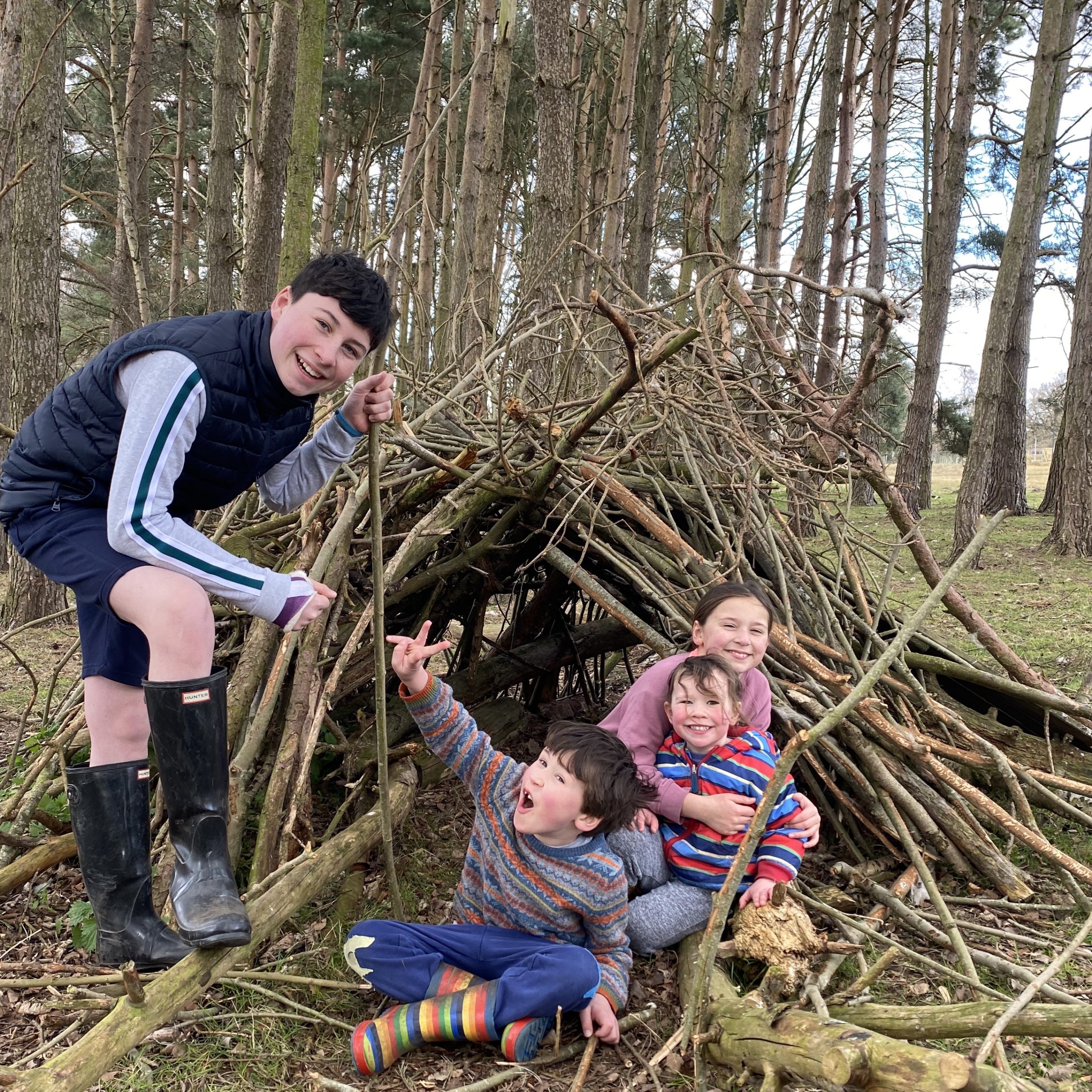 Four children playing in the woods with sticks 