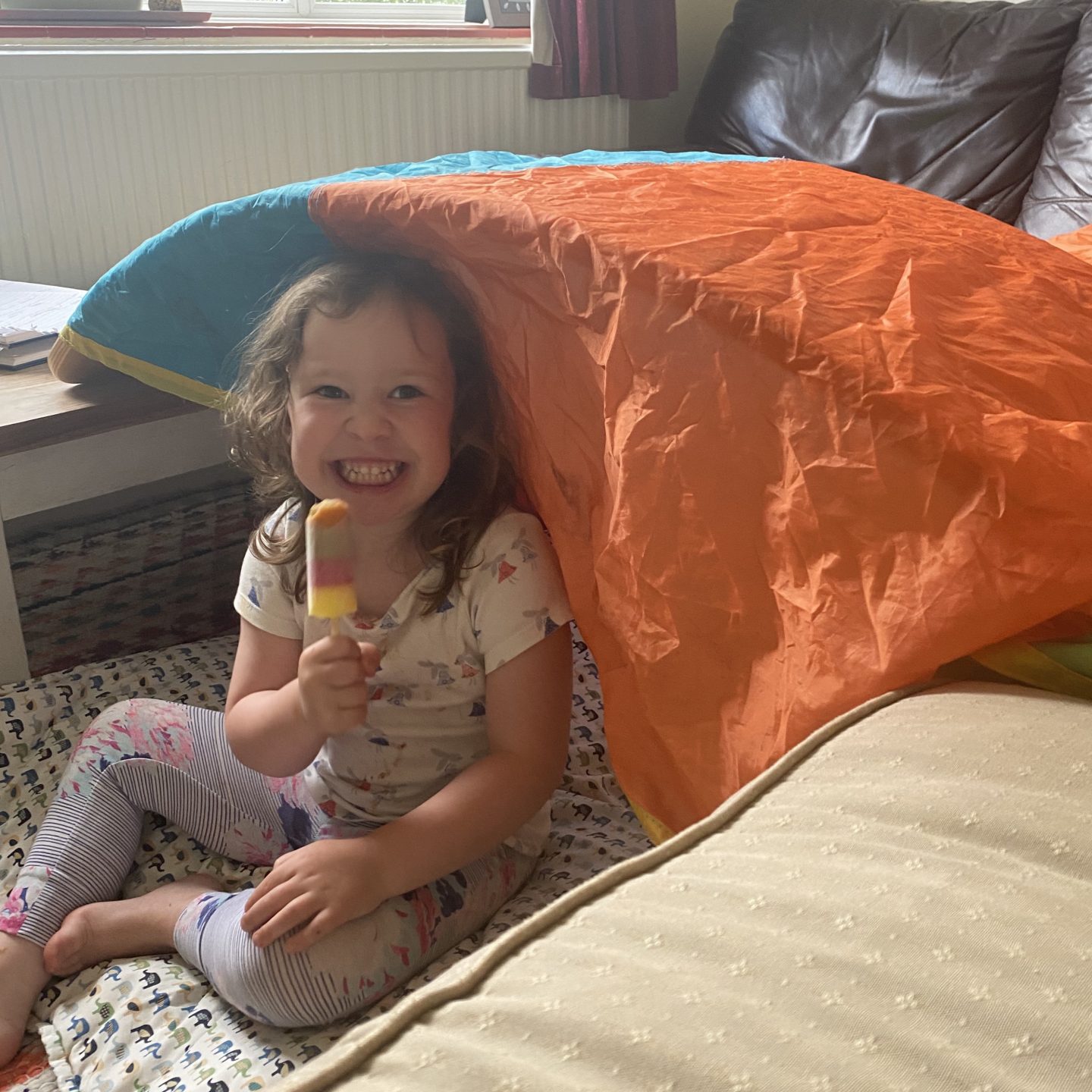 a young girl eating an ice lolly under a coloured parachute for Glasthomebury