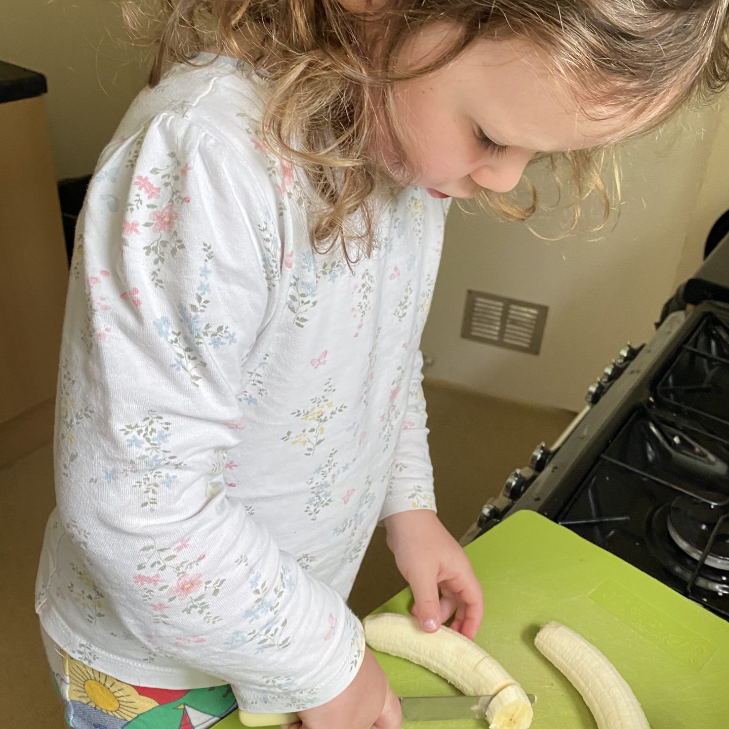 Organising for a family holiday with a child chopping a banana in the kitchen