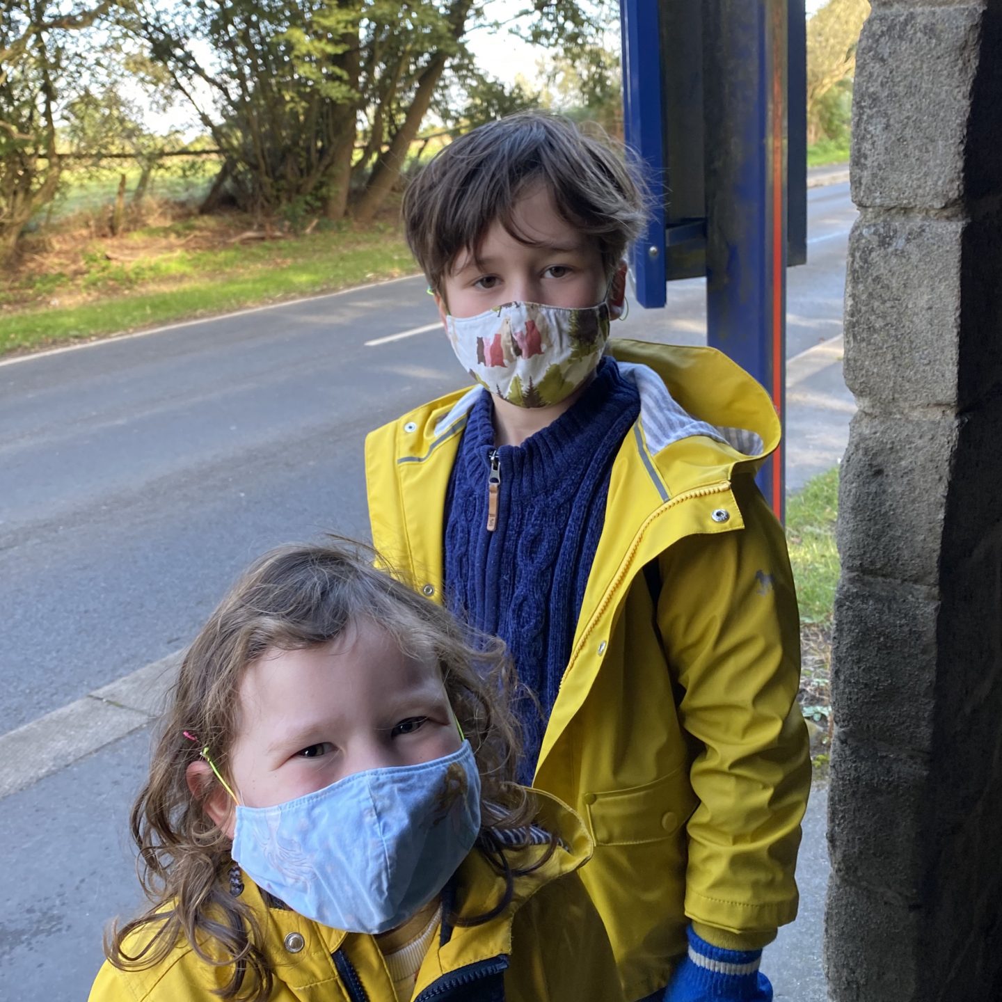 Two children stood at the bus stop wearing face masks