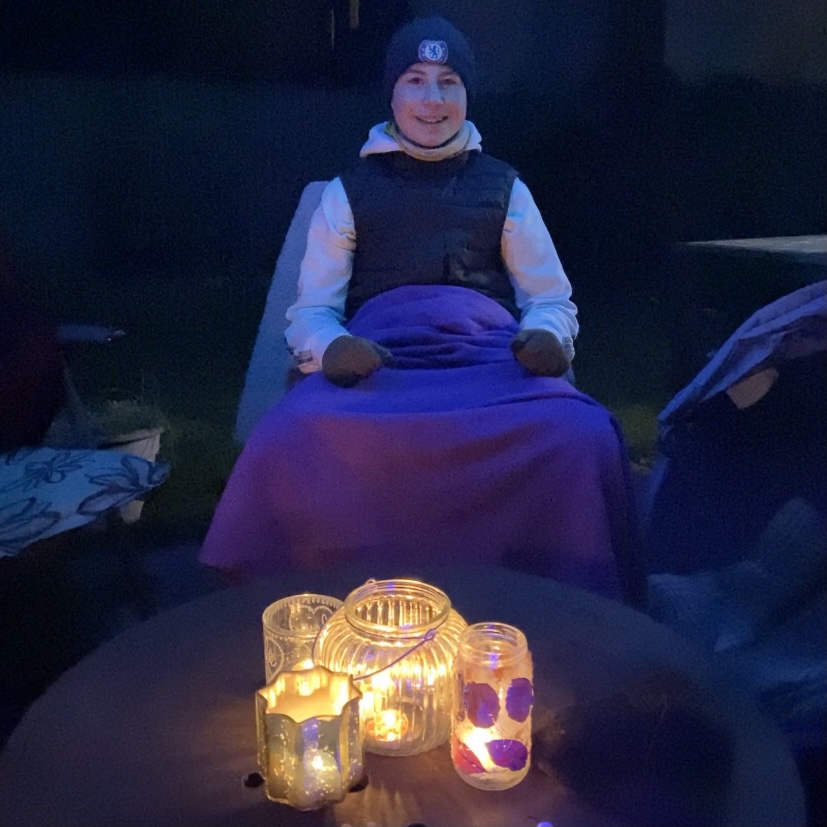 A boy sat outside round a bonfire in the dark 