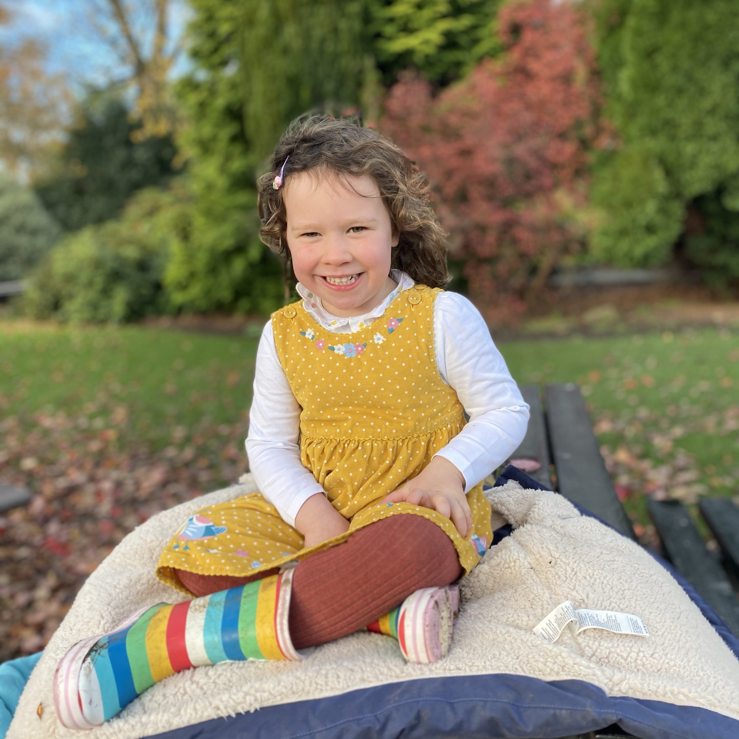 a little girl sat smiling on a picnic bench in the park 