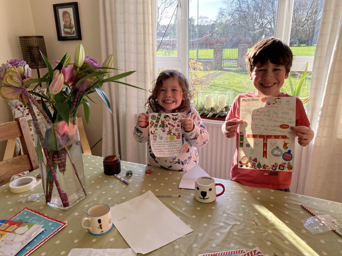 two children writing letters to Santa holding them up and smiling 
