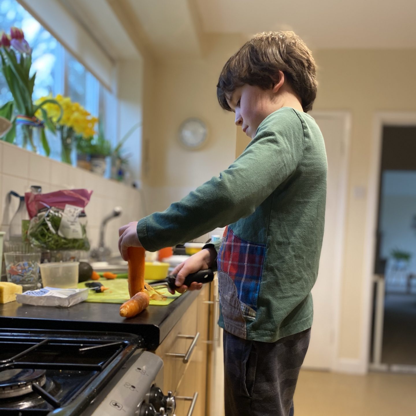 A boy helping in the kitchen peeling a carrot