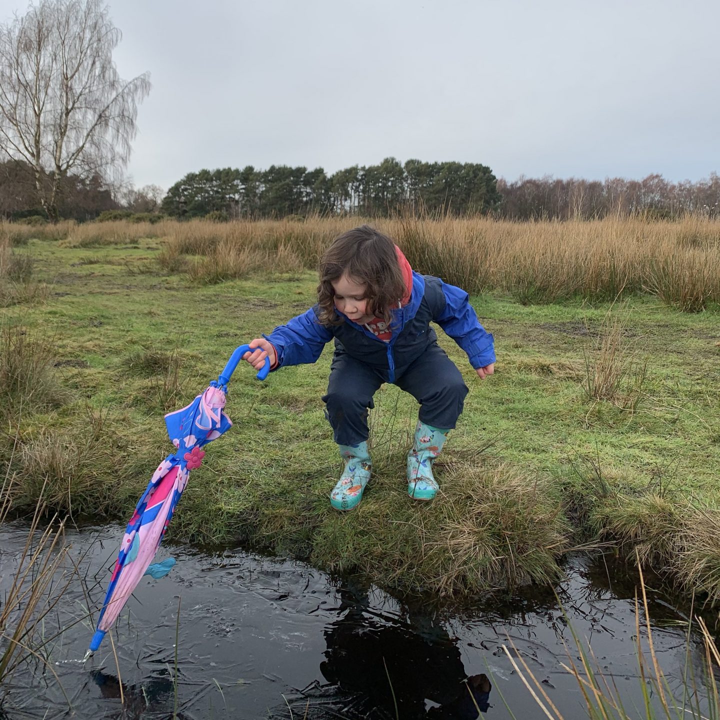a young girl poking an umbrella in a ditch 