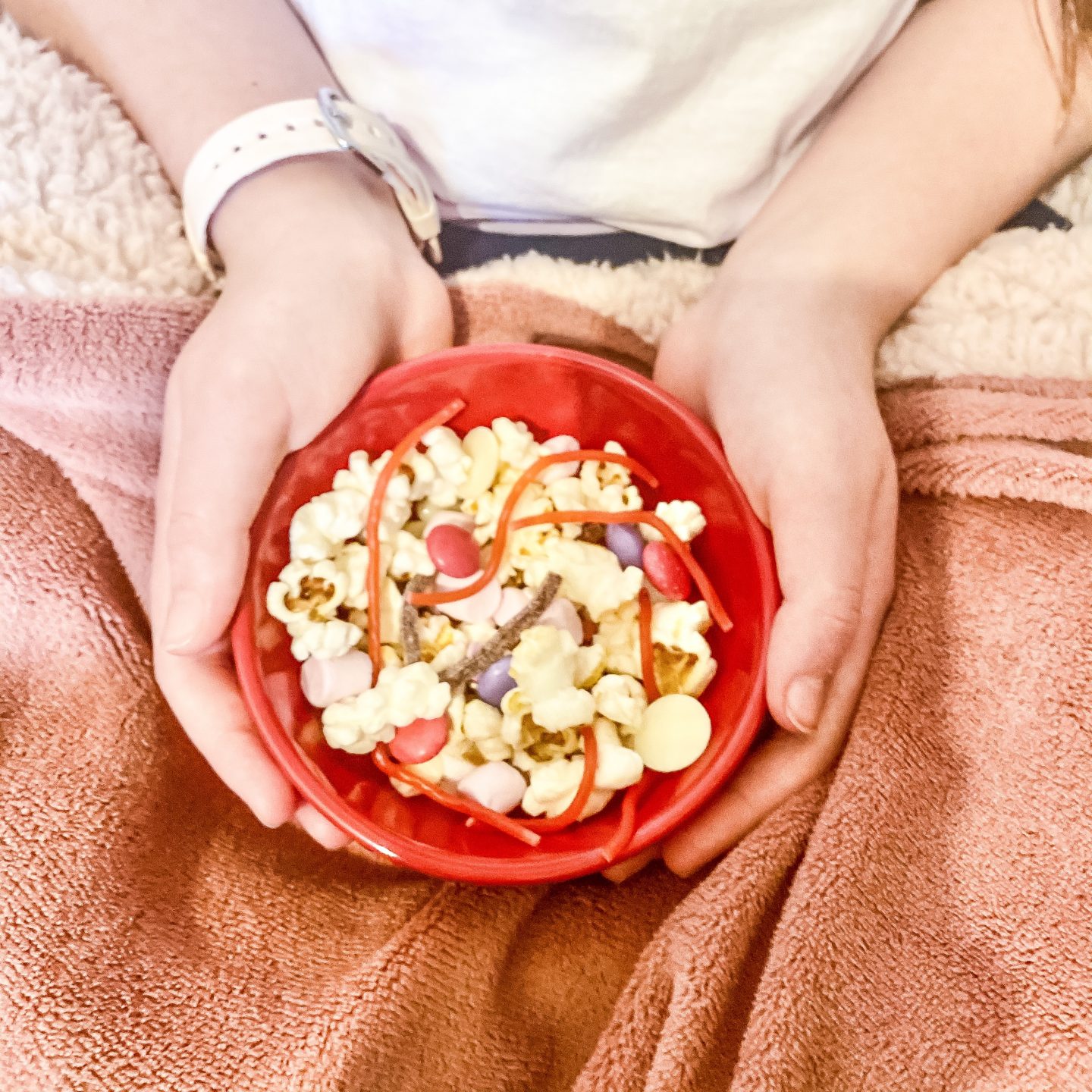 valentine's movie snack mix with a girls sat holding a bowl of movie snacks with popcorn and sweets 
