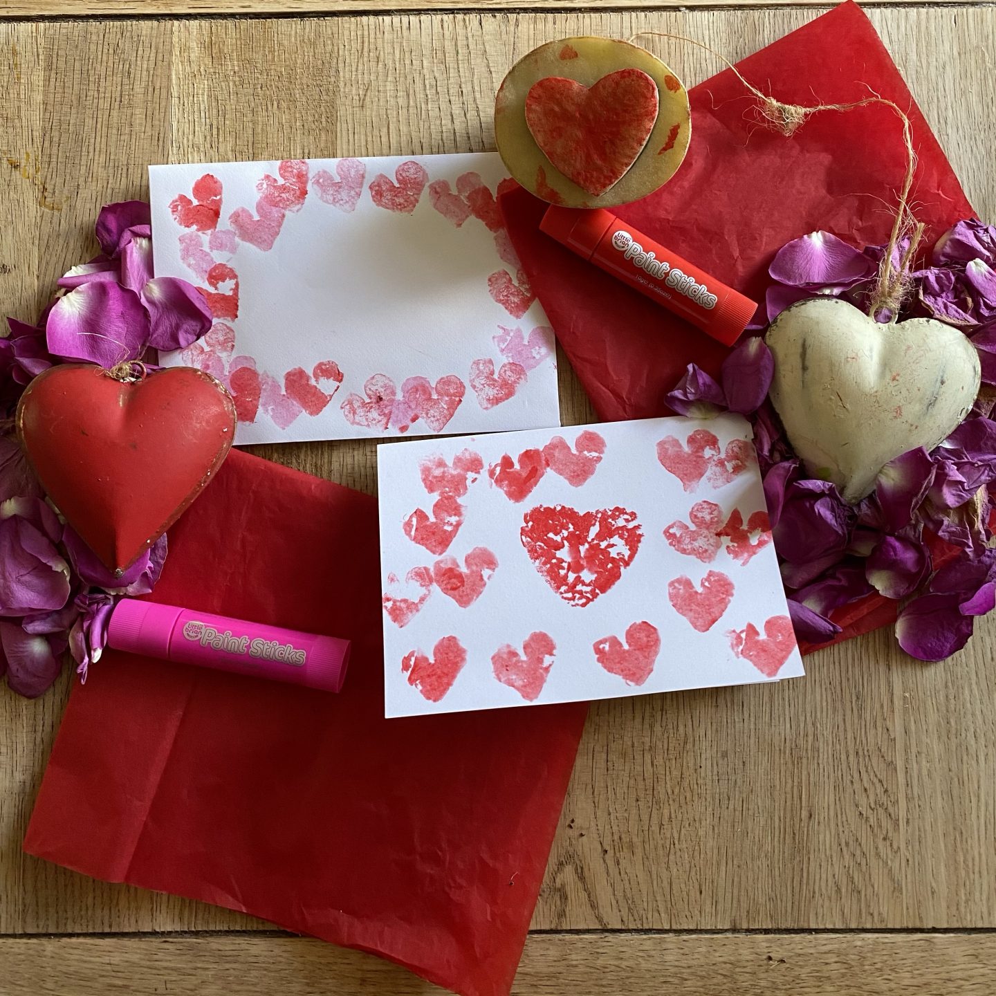 potato stamping hearts on an envelope and card with paint sticks, Hearst and petals on a table 