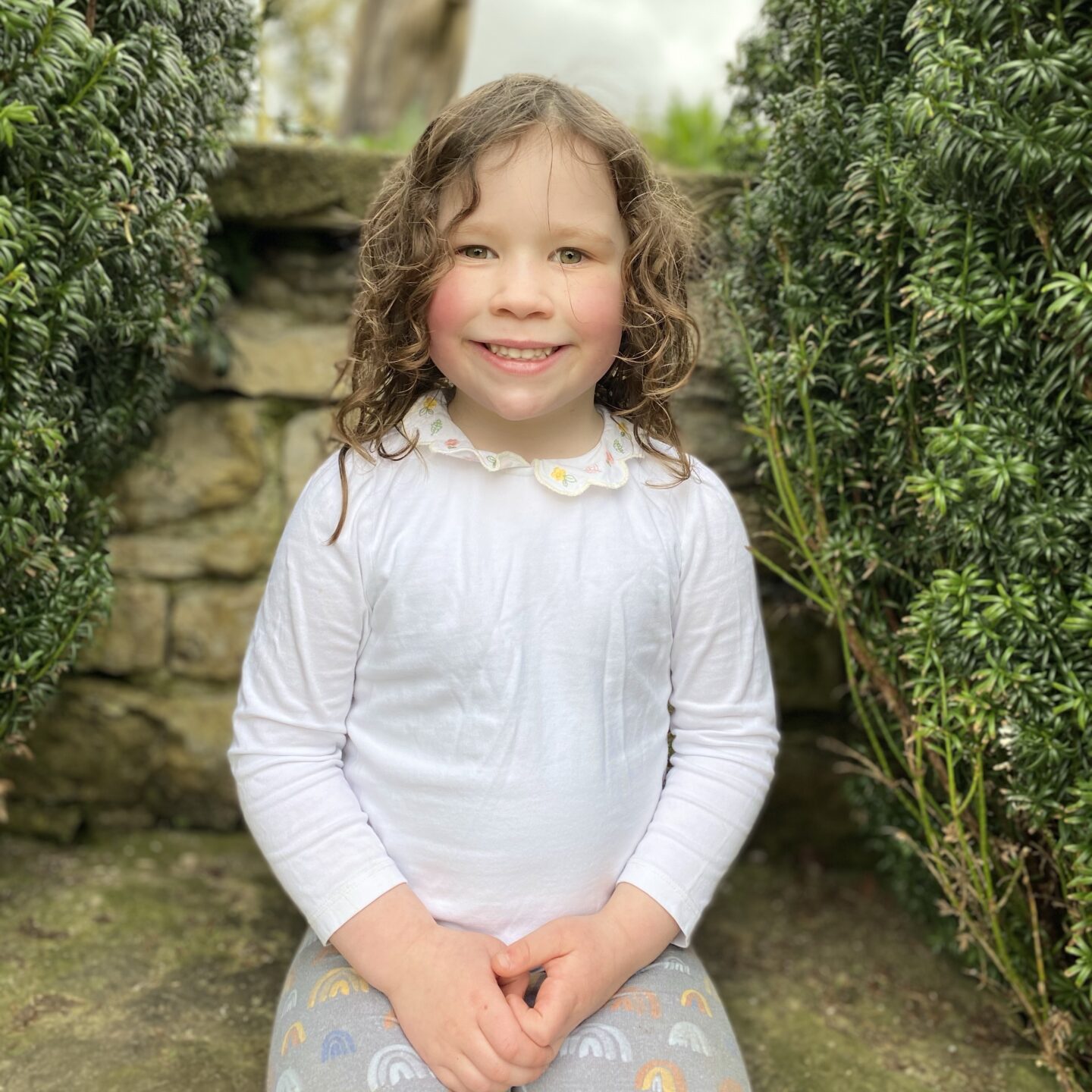 a young girls sat in the garden smiling at the camera