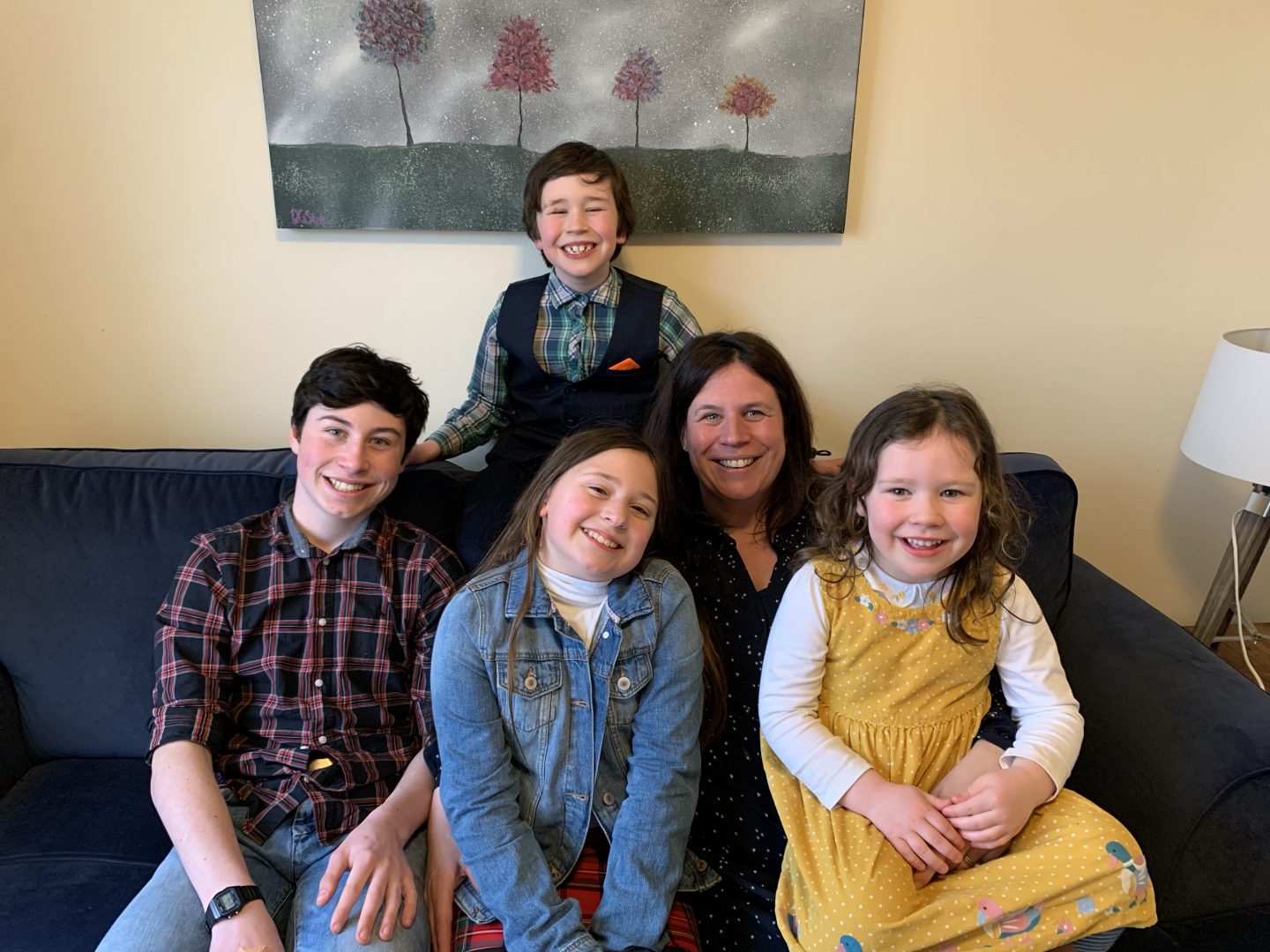 A mum and 4 children sat on a sofa smiling for the camera
