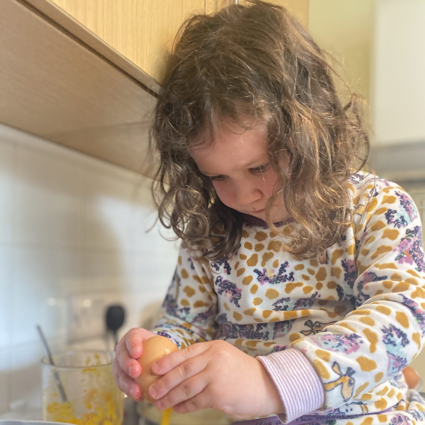 rainy may activities with a small child cracking an egg in a cup whilst baking