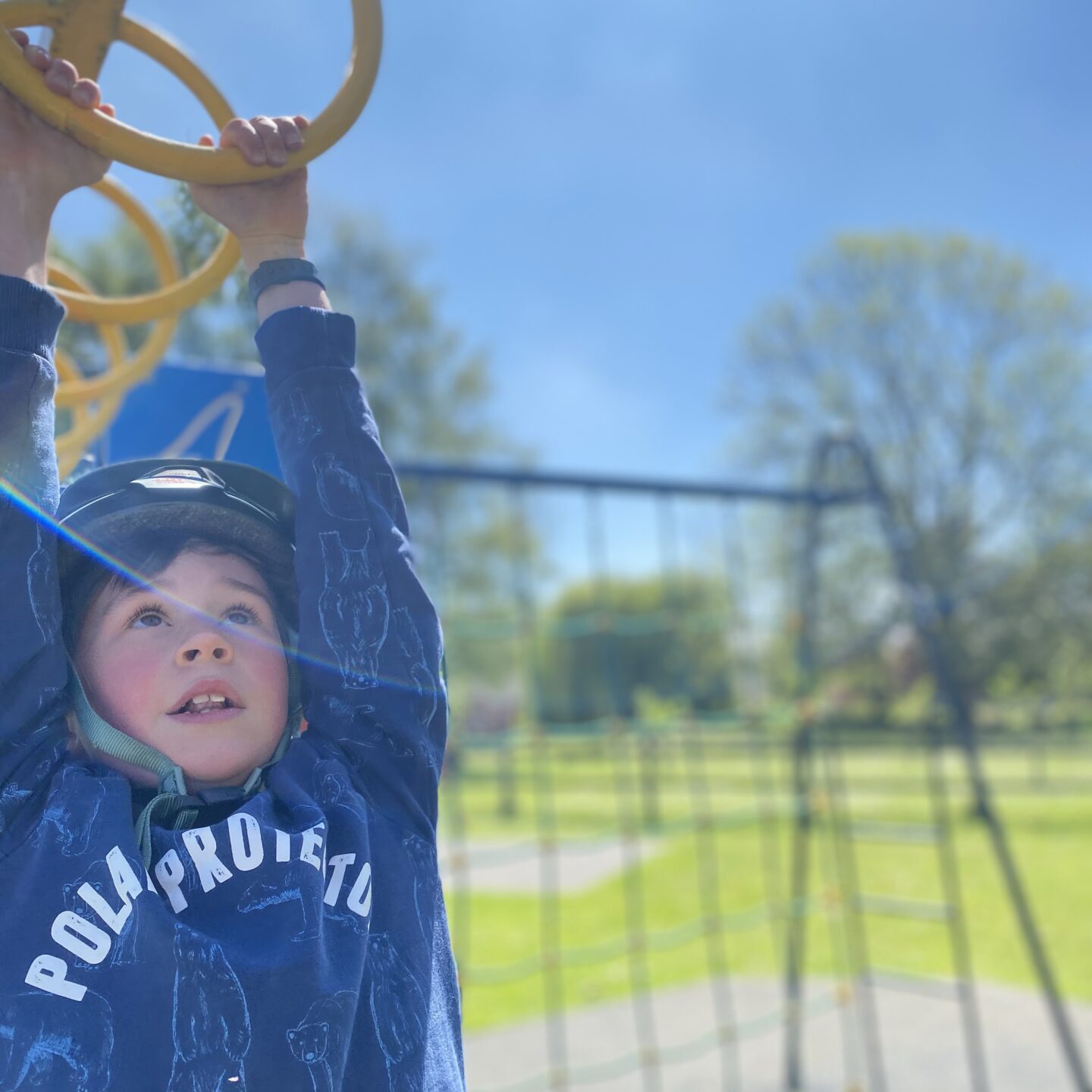 A boy hanging off the monkey bars in the park