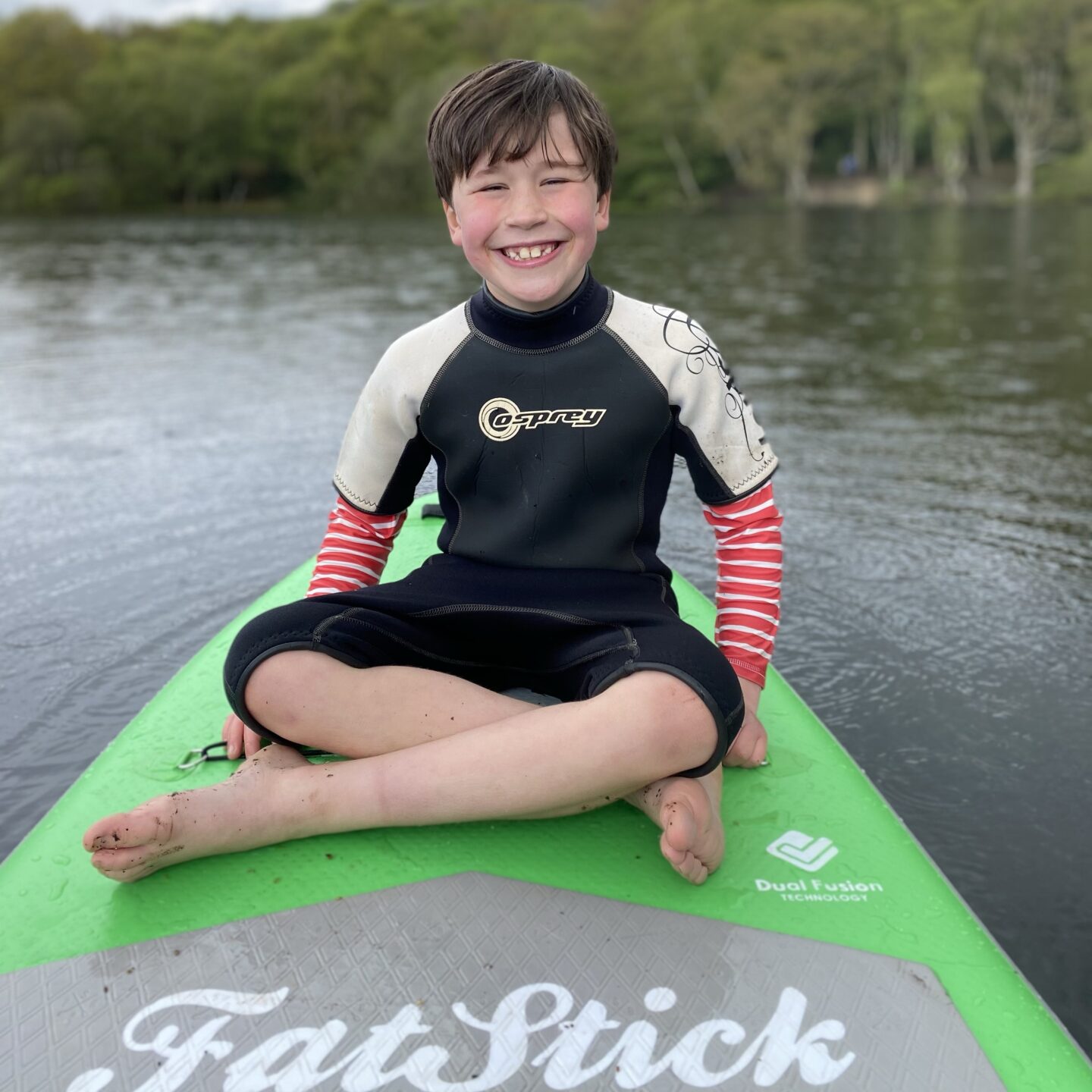 a boy sat smiling on a paddle board on Lake Gormire