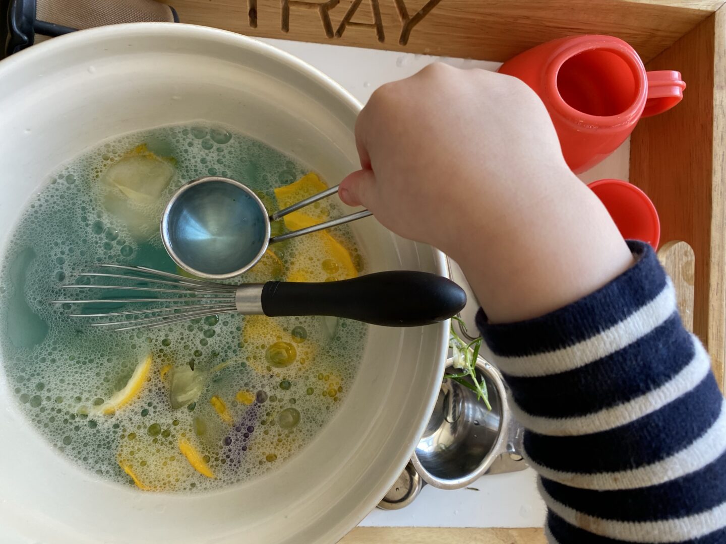 a child making flower petal soup with bubbles and a whisk in a bowl