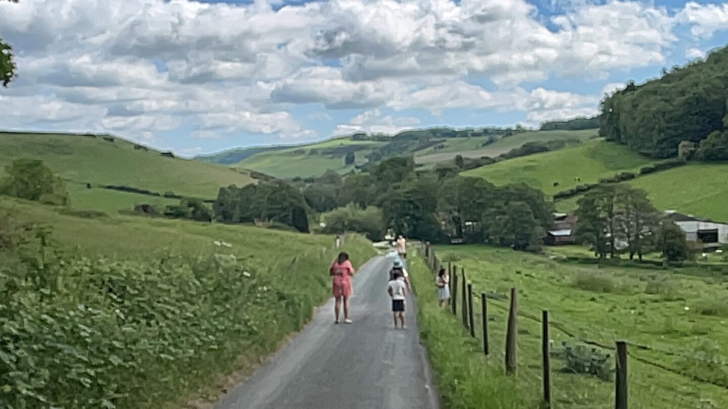 A view of rolling green hills and a family walking down a farm track