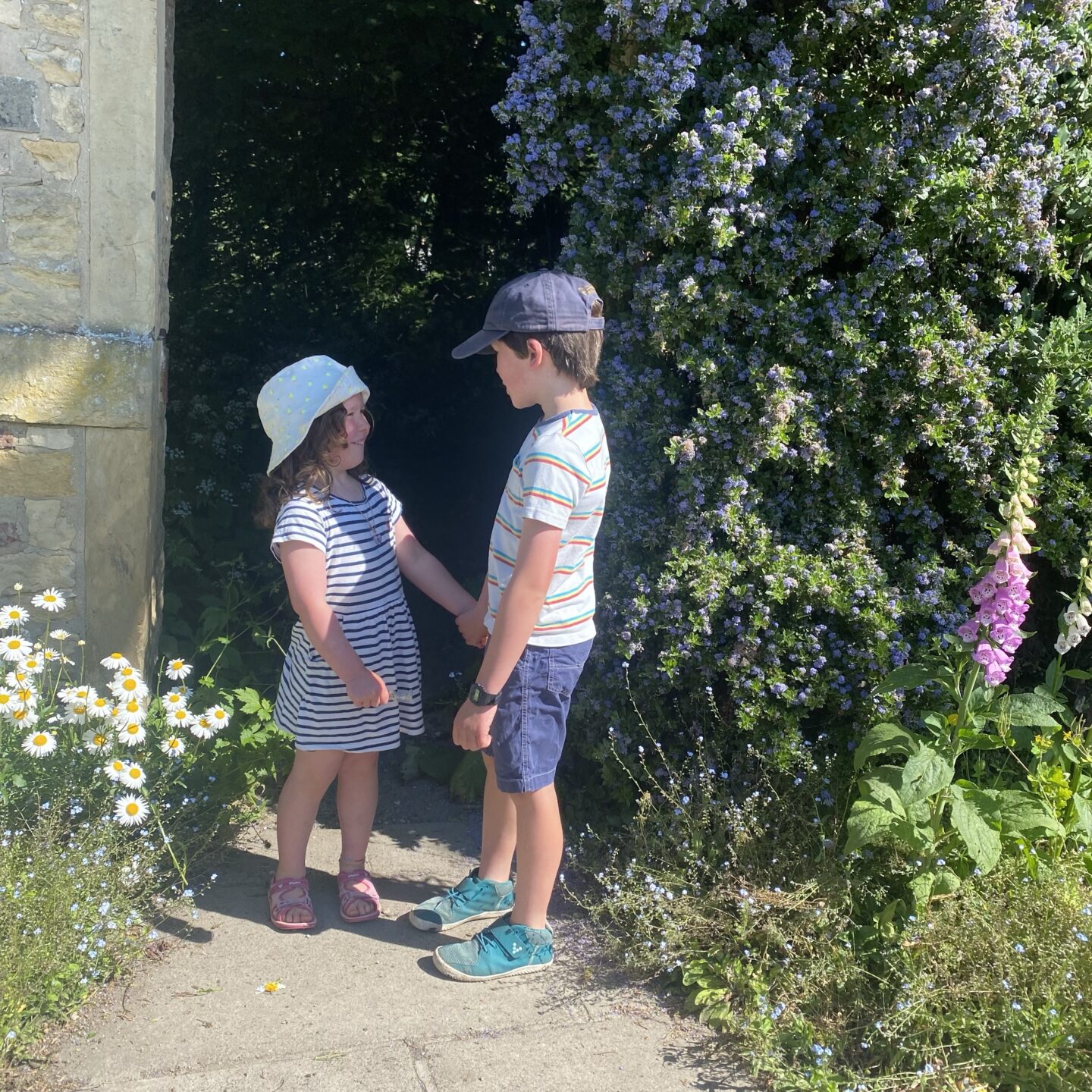 Two young kids looking at each other around flowers