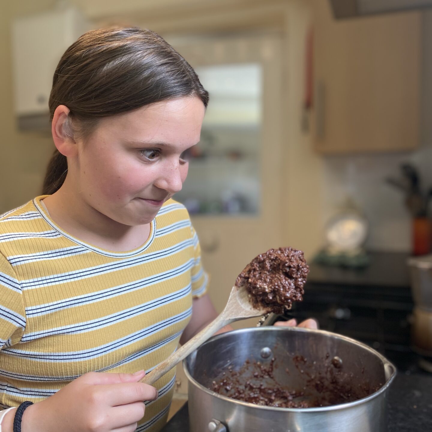 family life with a girl baking and smiling at a saucepan of melted chocolate