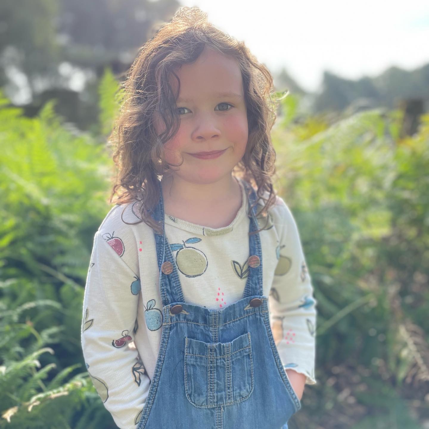 a young girl with hands in her pocket smiling at the camera