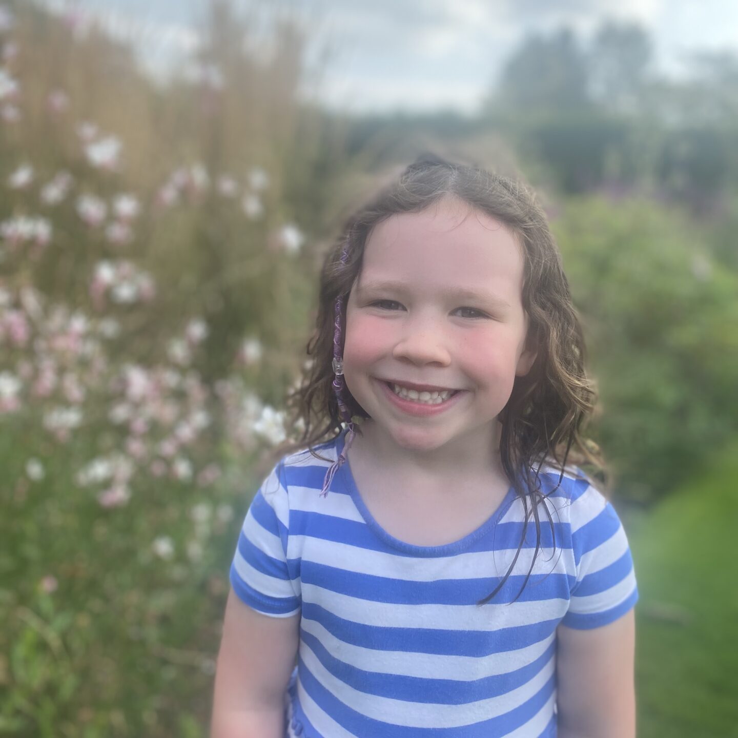 a small girl smiling at the camera by flowers 