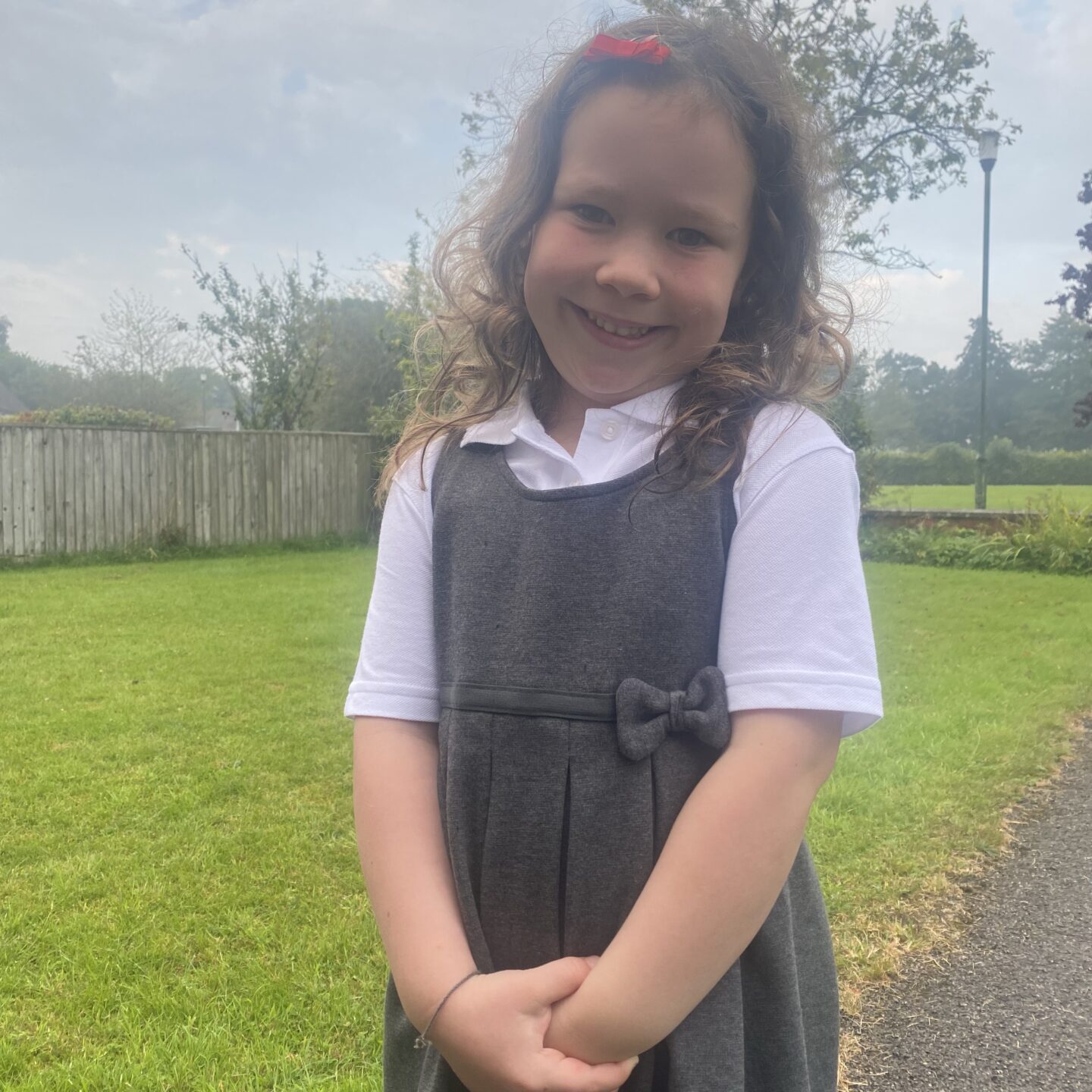 a young girl stood smiling at the camera in her uniform as she is starting school