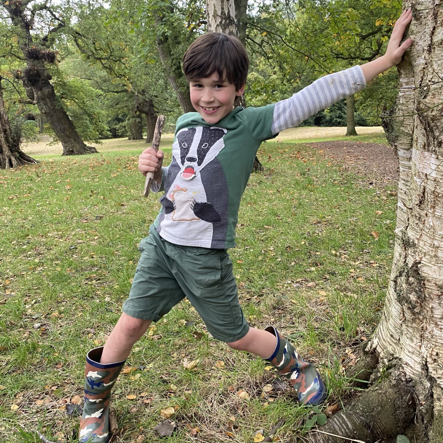 a boy wearing a badger top by a tree