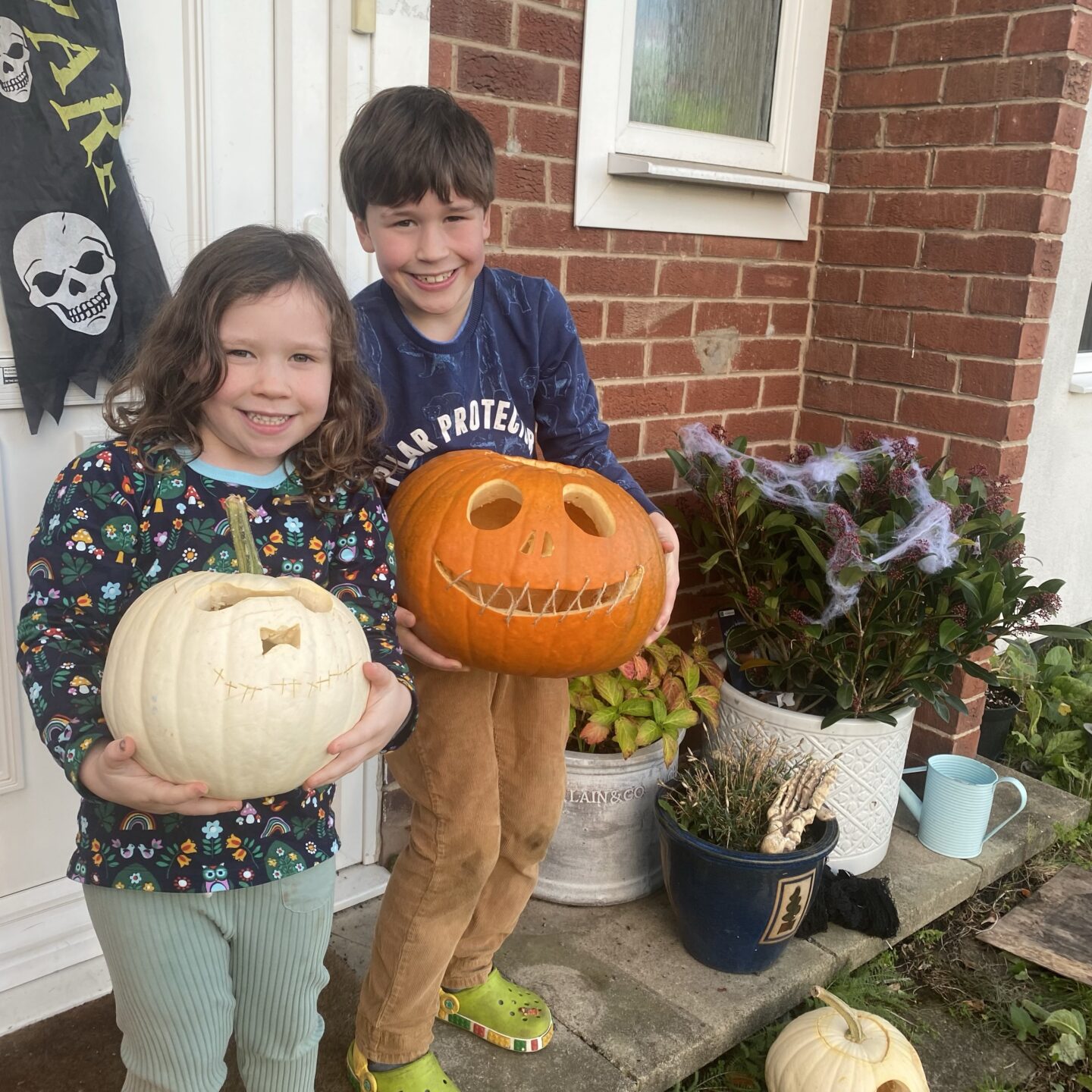 two kids holding carved pumpkins on the doorstep