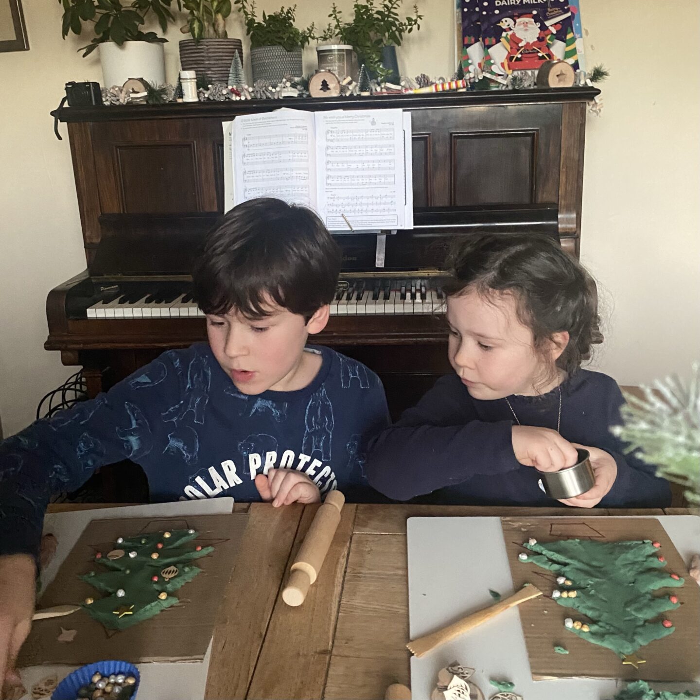 two children sat at a table making play dough Christmas trees
