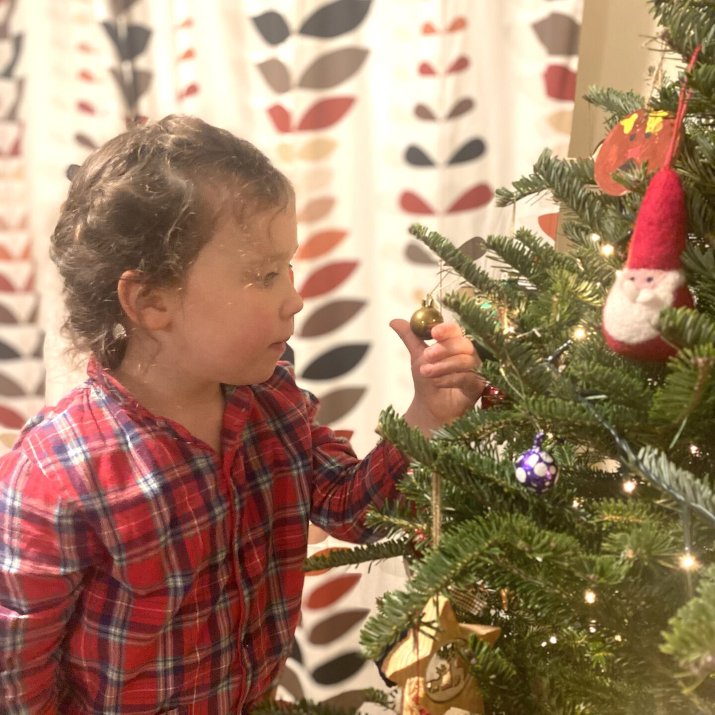 a girl looking at a bauble on a Christmas tree