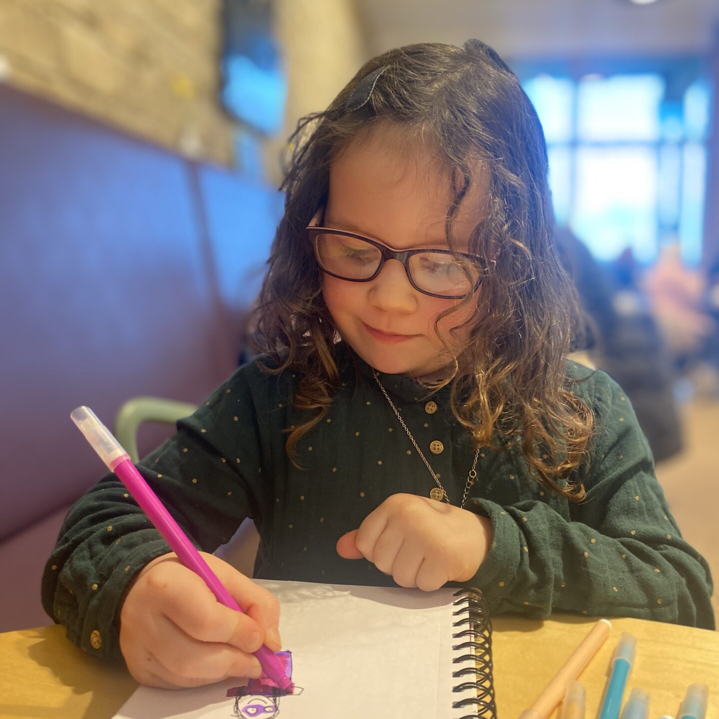 a young girl sat drawing in a cafe 