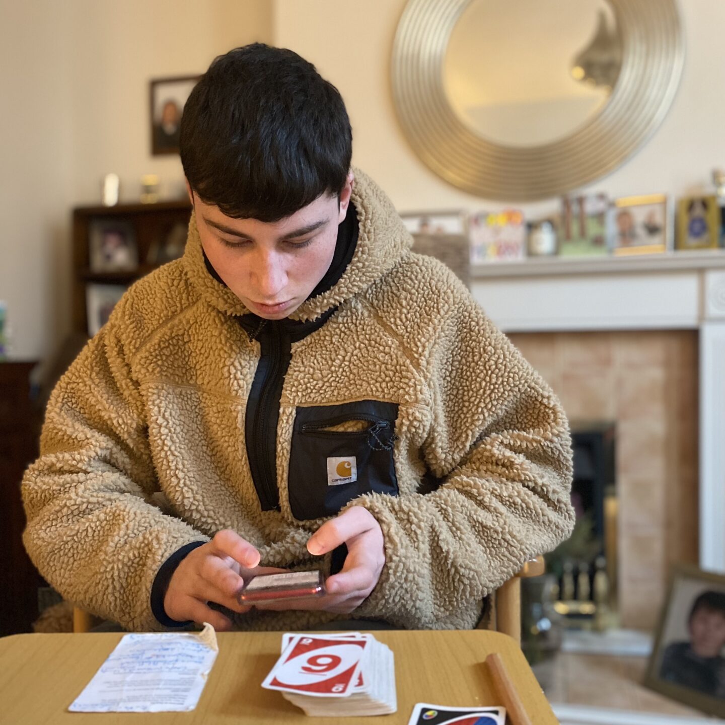 a teenage boy on his iPhone whilst playing cards