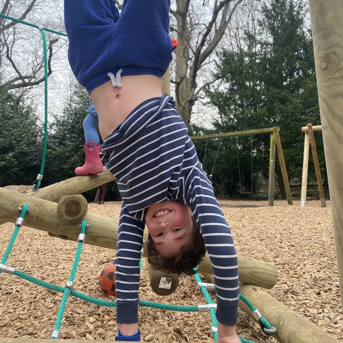 A young boy upside down on a climbing frame at the park