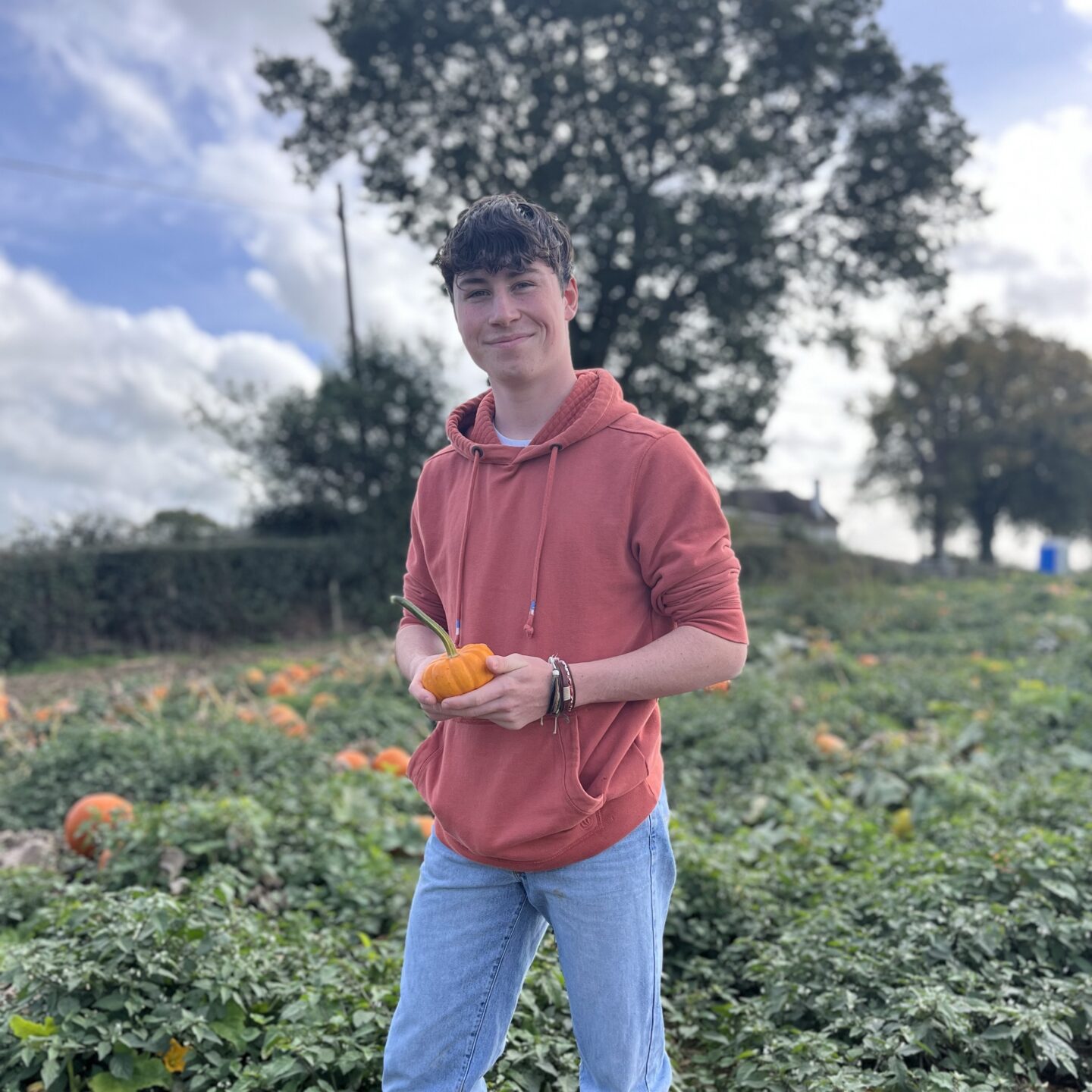 Teenage boy holding a tiny pumpkin in a field