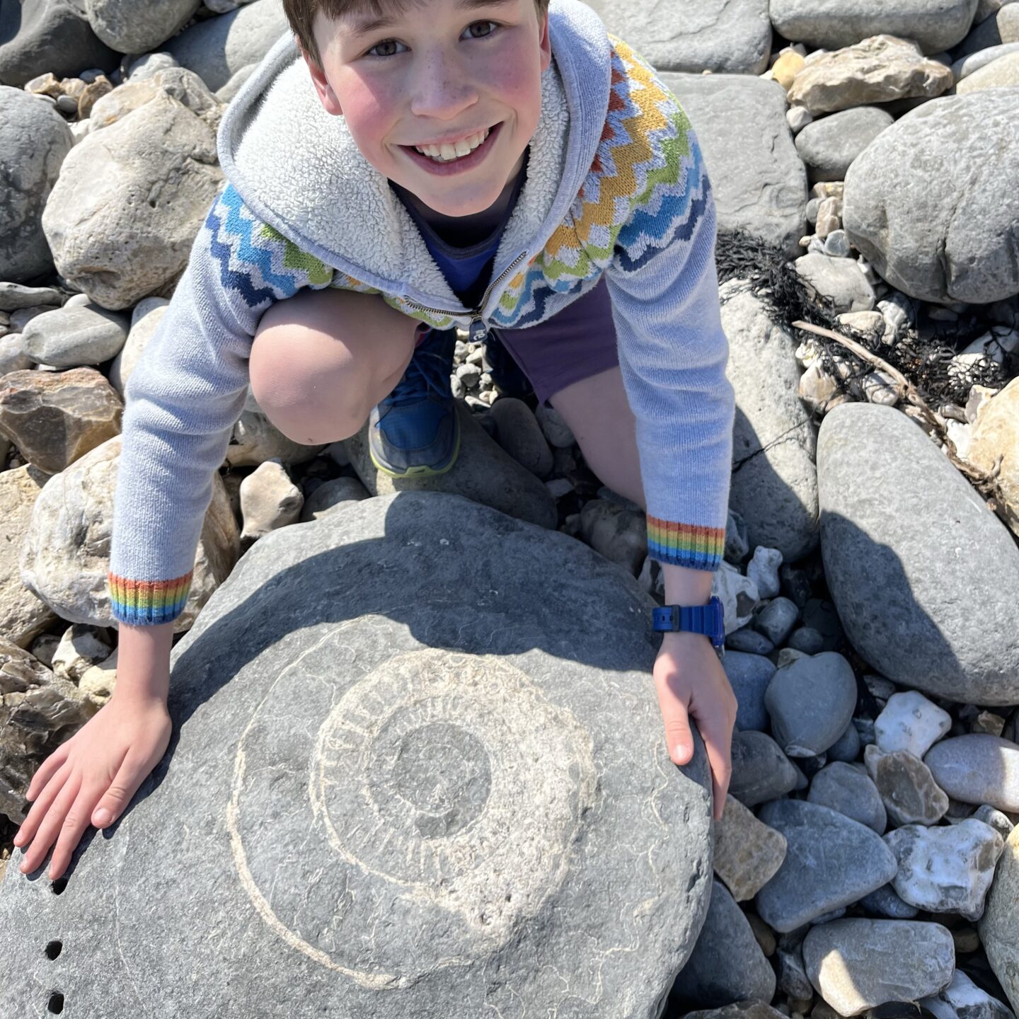 a boy smiling at a huge an ammonite 