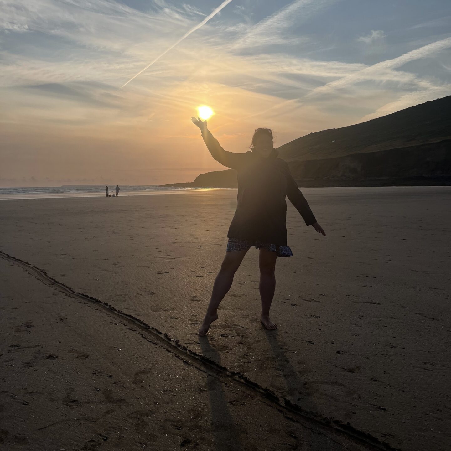 a lady on the beach at sunset pointing to the sun 