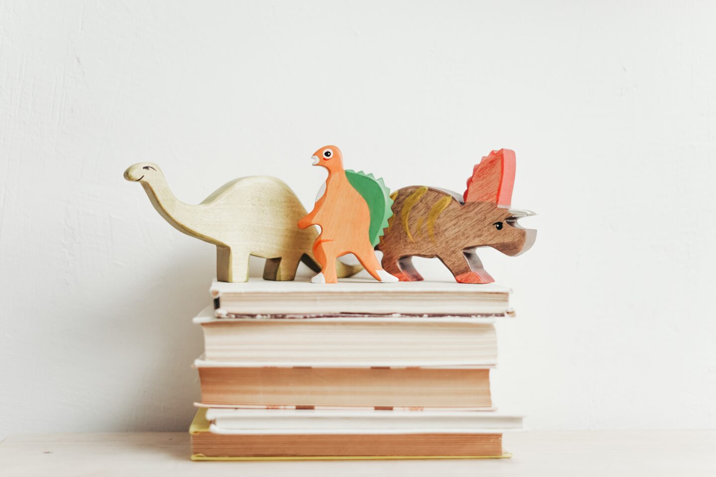 how to raise a hardworking child with books piled up with wooden dinosaurs on top